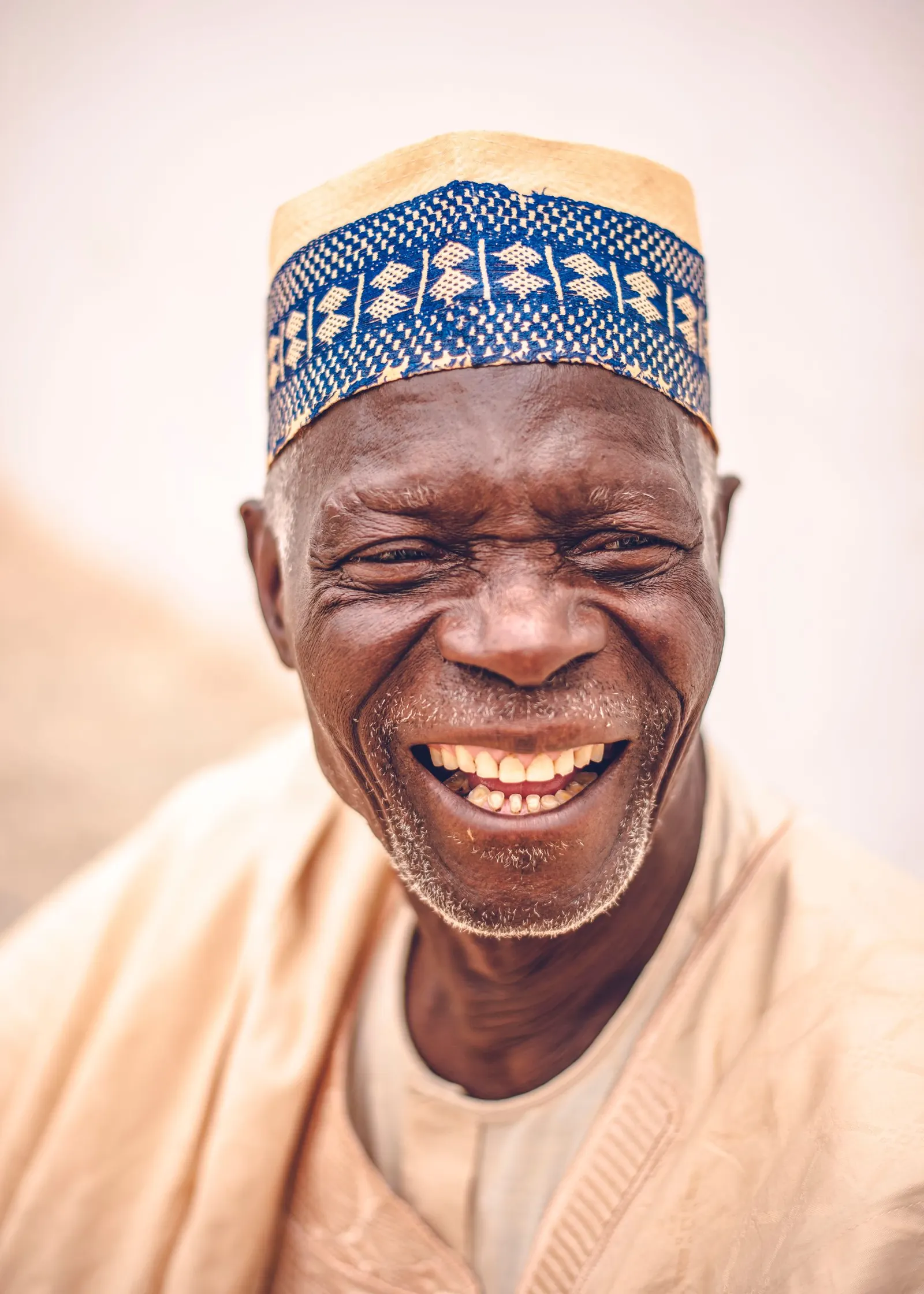 Elderly Nigerian man in an embroidered cap laughing warmly