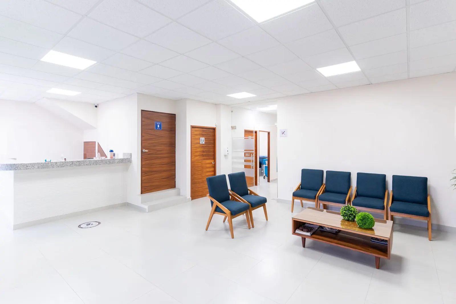 Bright, clean clinic waiting area with blue chairs, a low table and the reception counter